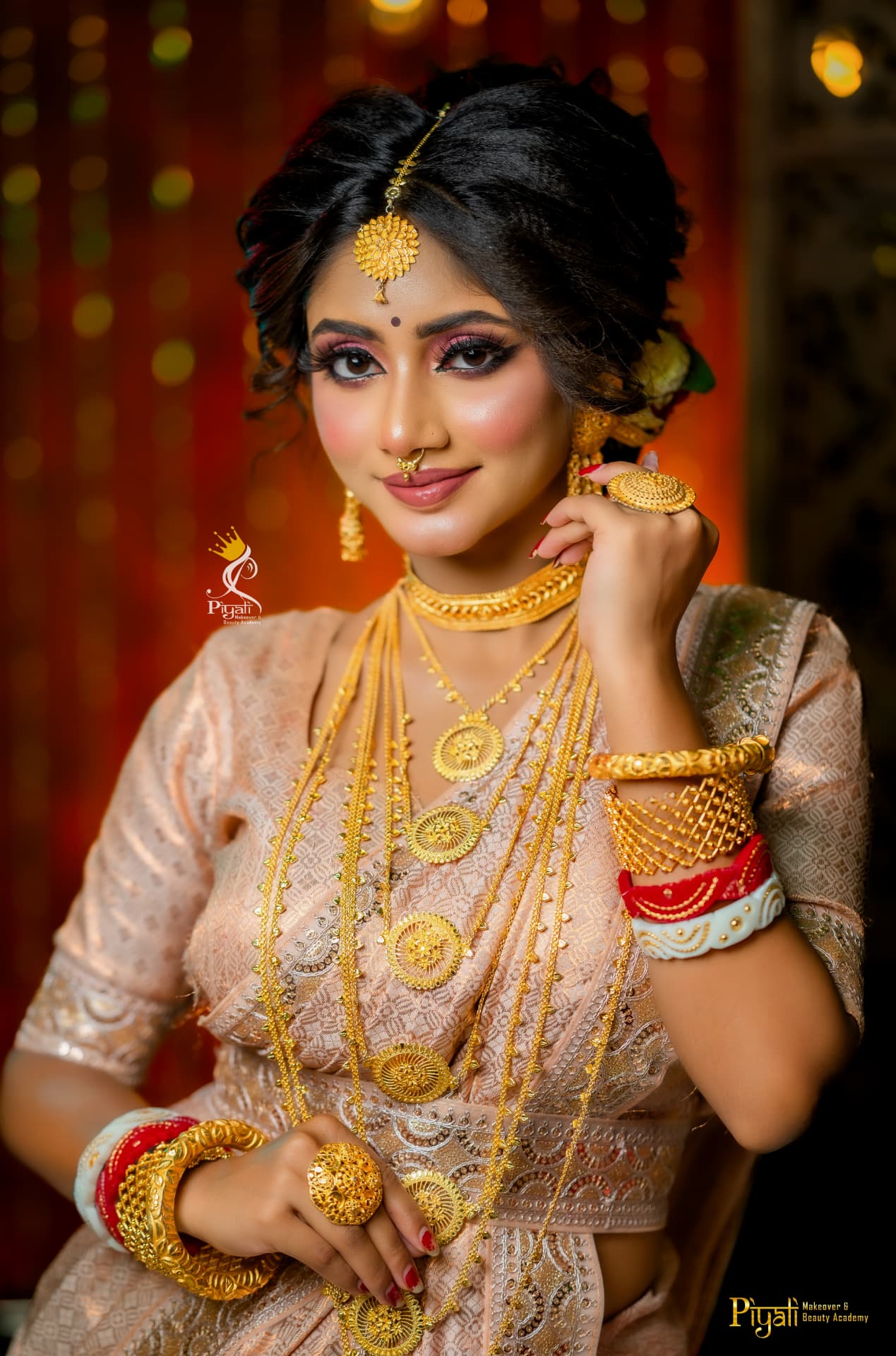 Bride in a blush peach sari draped in layered gold chains with statement bangles and rings