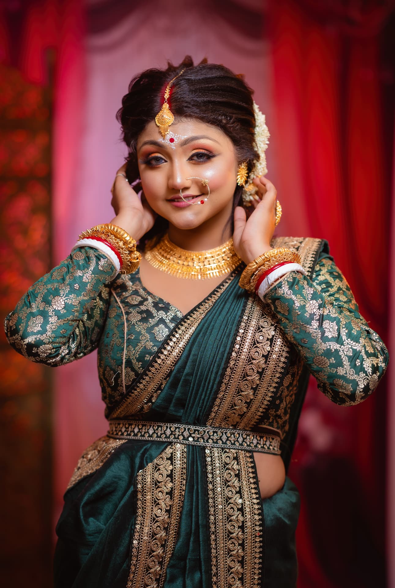 Bride in an emerald green brocade sari with a gold belt and choker against a rose-lit backdrop