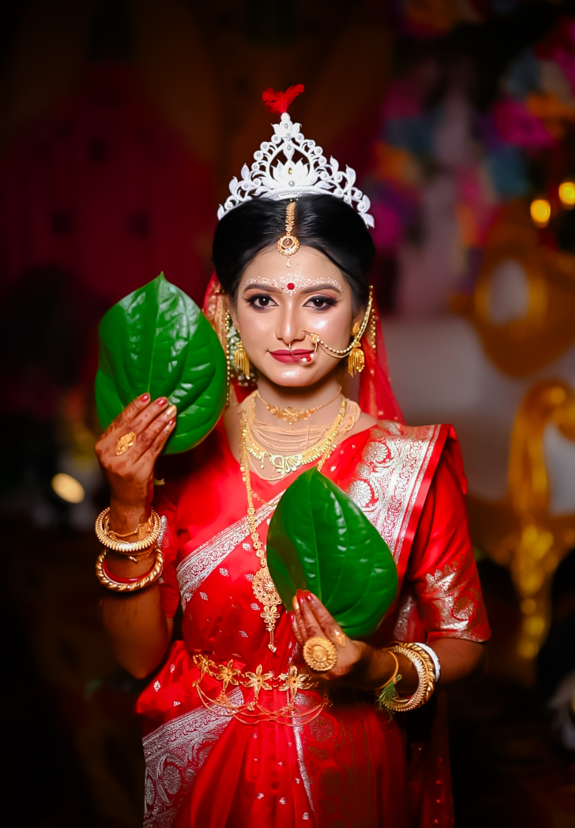 Bride in a red benarasi with gold jewellery holding betel leaves