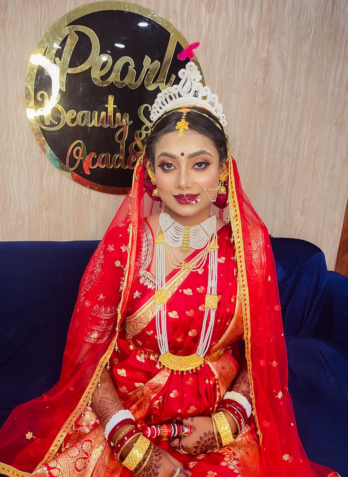 Bengali bride seated before the Pearl Beauty Salon & Academy sign after her bridal makeover